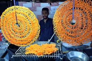 A vendor preparing the traditional sweet food item (Jalebi) to the customer on the roadside setup in the Provincial Capital.