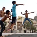 Children enjoying and jumping on trampoline along the roadside during hot weather in the city