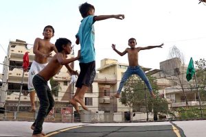 Children enjoying and jumping on trampoline along the roadside during hot weather in the city