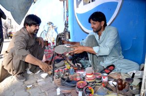 - Cobbler preparing damaged shoos of its customer who sitting near him at Jinnah Road.