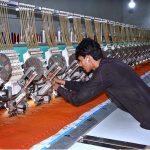 A worker monitors fabric embroidery on a computerized machine at a local factory
