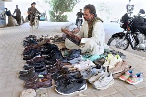 A vendor polishes used shoes displayed on the sidewalk to attract customers looking for low-priced footwear.