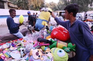 A vendor sells baby dolls and other toys from his handcart along the roadside in the city