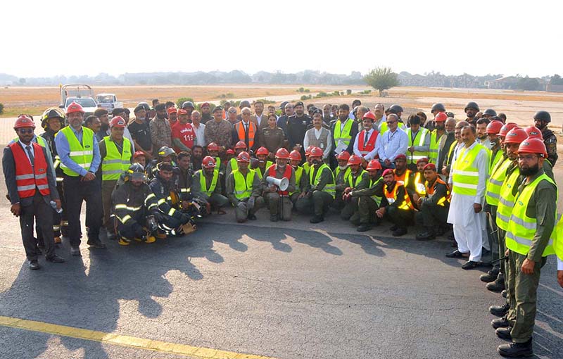 A group photograph of officials, emergency response personnel, Rescue 1122, fire brigade teams and security staff during a full-scale emergency exercise conducted by the Pakistan Airports Authority (PAA) at Multan International Airport to evaluate operational readiness and equipment functionality